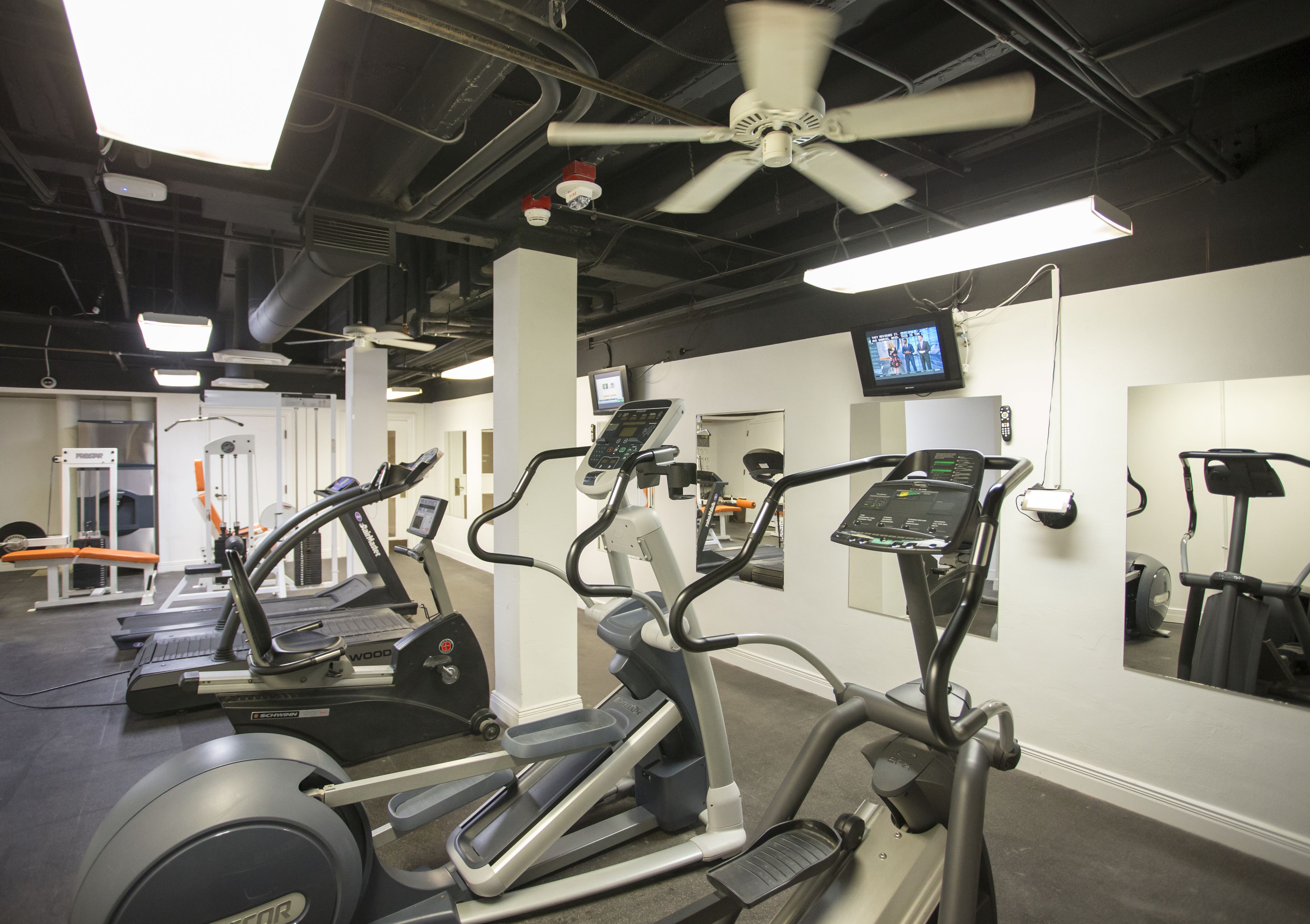 A gym with treadmills, elliptical machines, and a ceiling fan.