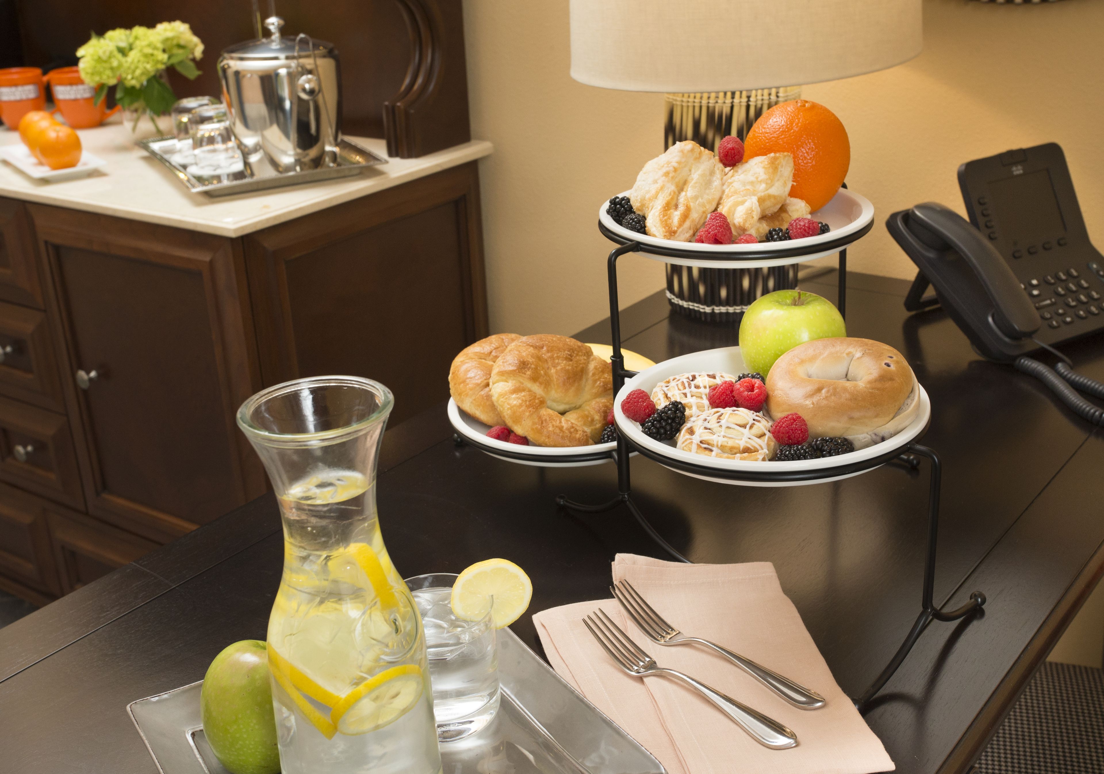 A breakfast setup with croissants, berries, and a pitcher of lemonade on a hotel table.