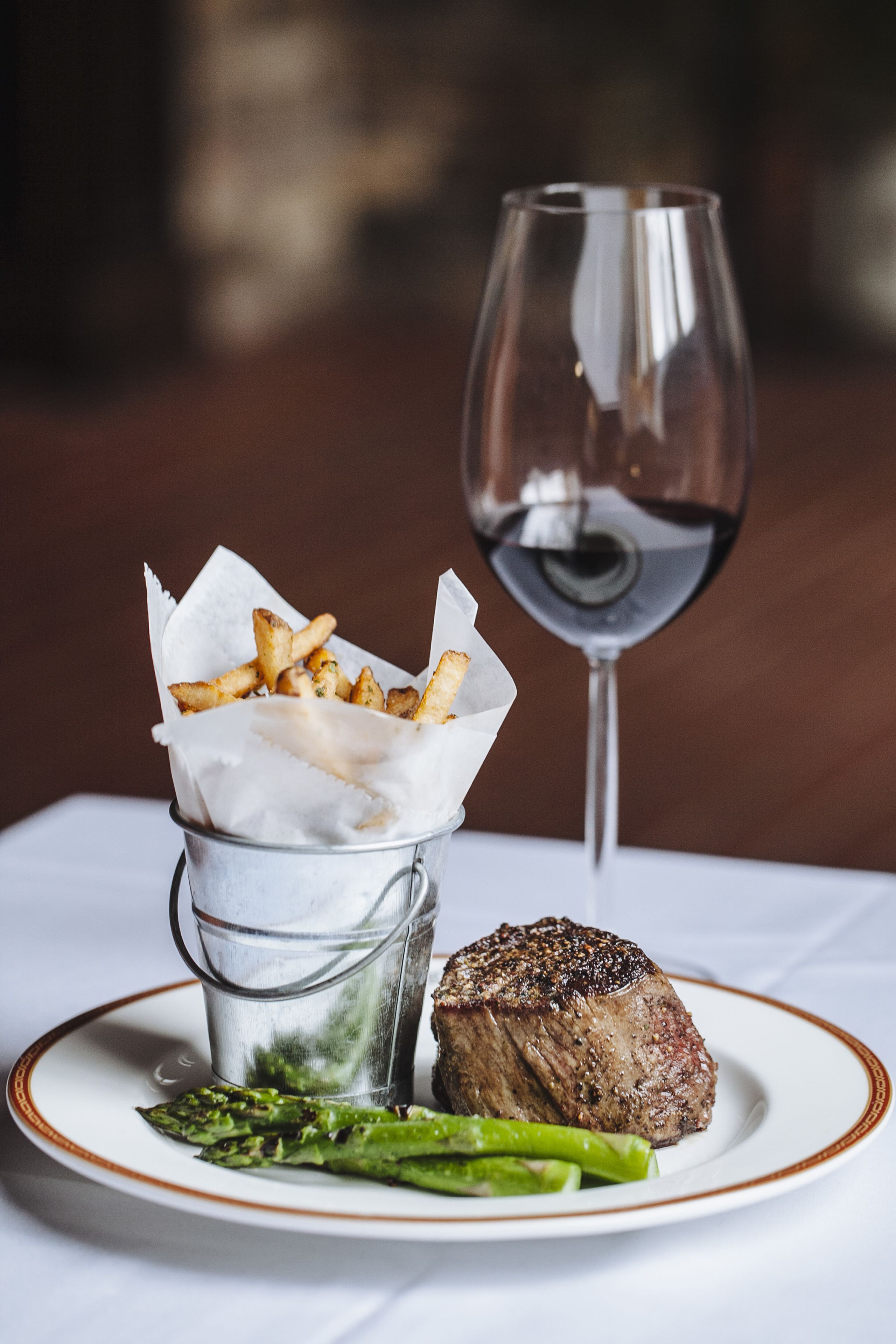 Een bord met steak, asperges, friet en een glas rode wijn.