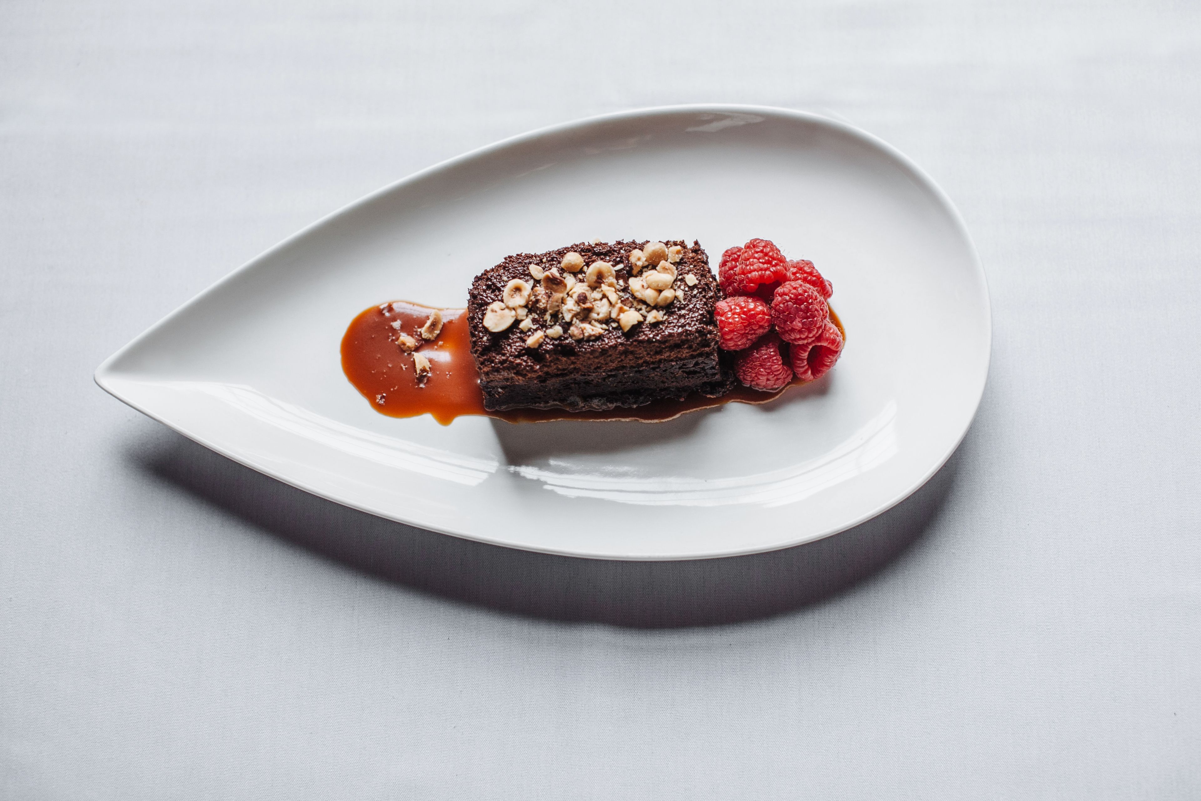 Un dessert servi dans une assiette blanche, accompagné d’une sauce et de framboises.