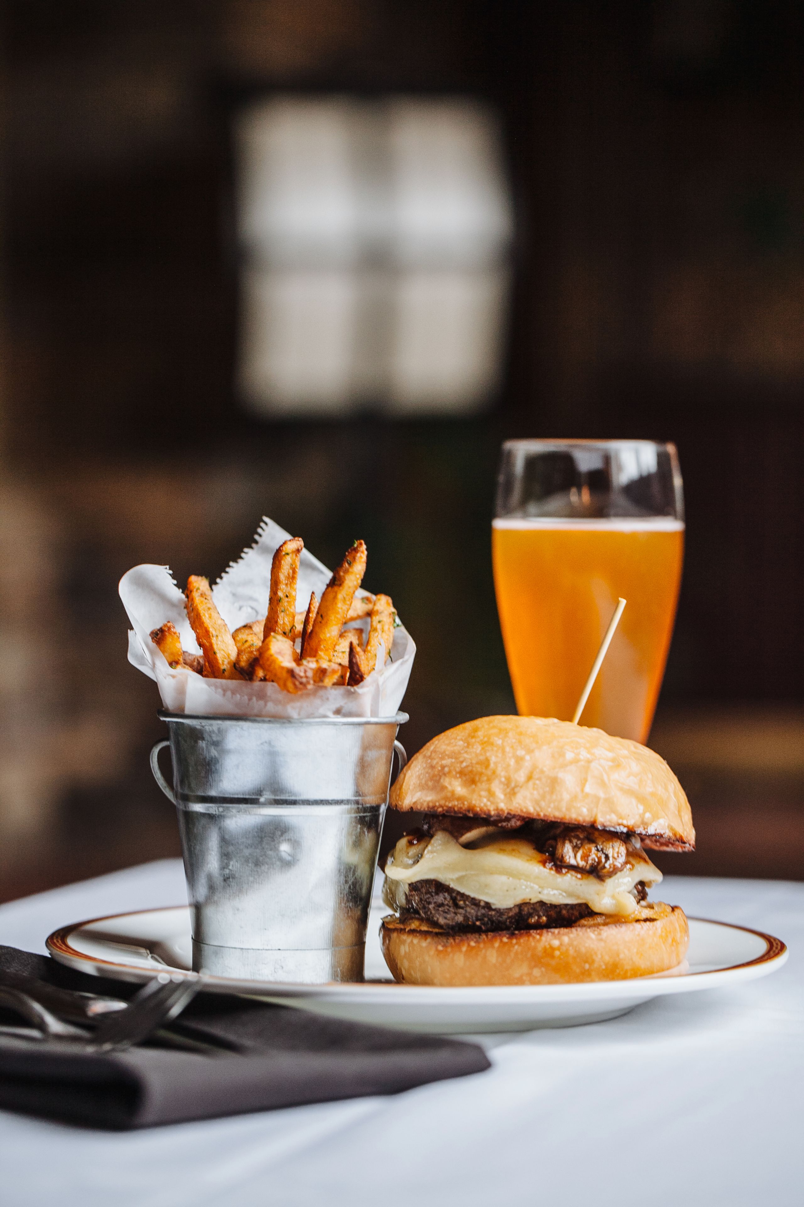 A meal consisting of a burger and fries on a white plate, with a glass of beer in the background.