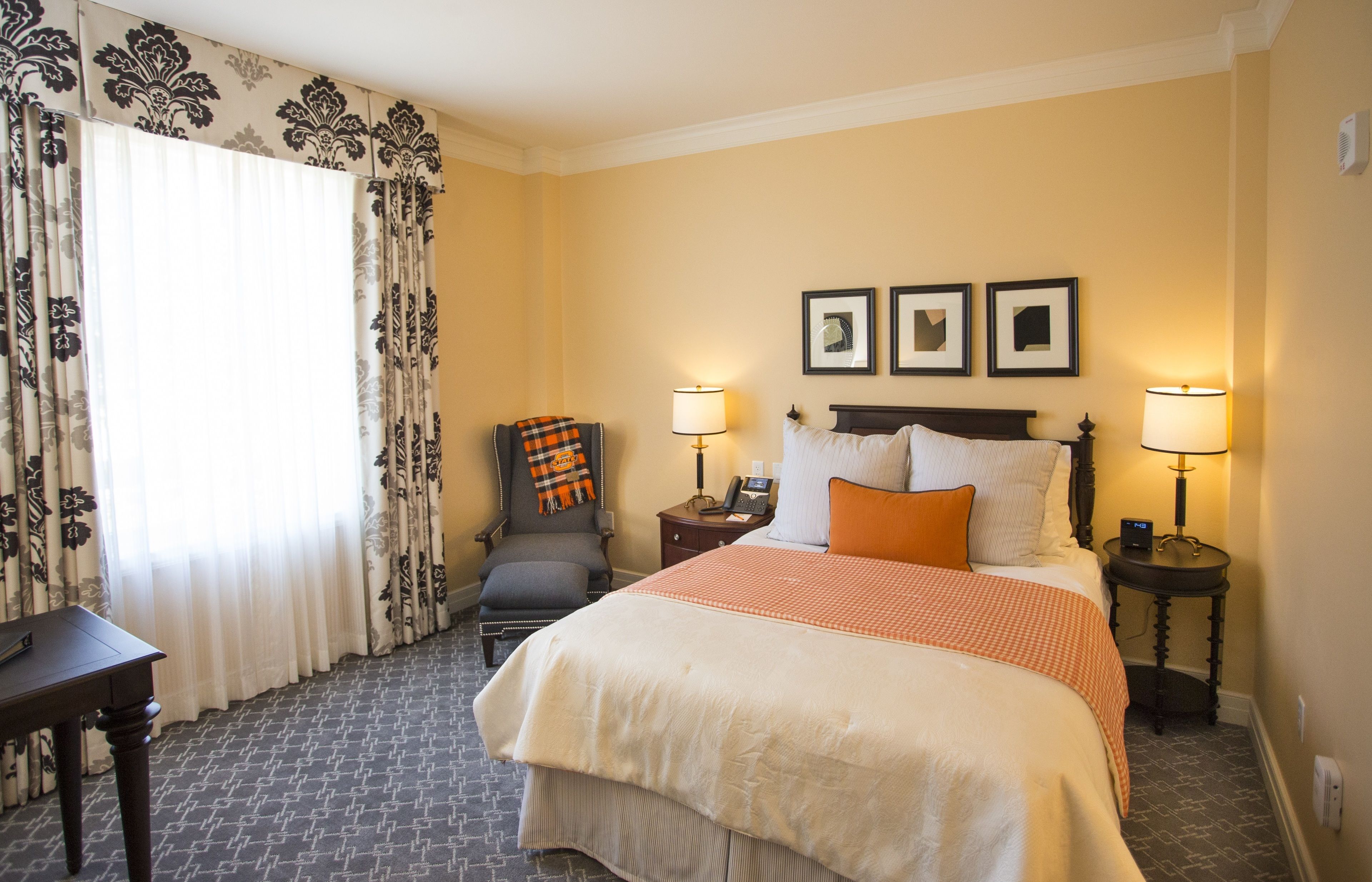 A hotel room with a large bed, two bedside tables with lamps, a chair, a desk, and a window with curtains.