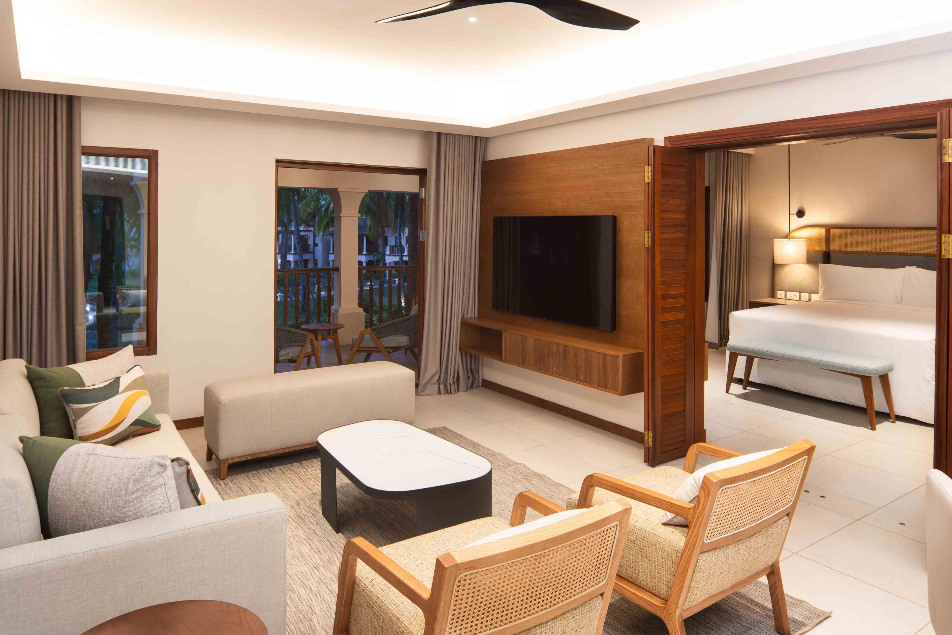 A modern hotel room with a sofa, armchair, flat-screen TV, and a bed.