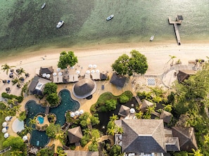 An aerial view of a resort with a beach, swimming pool, and thatched-roof structures.