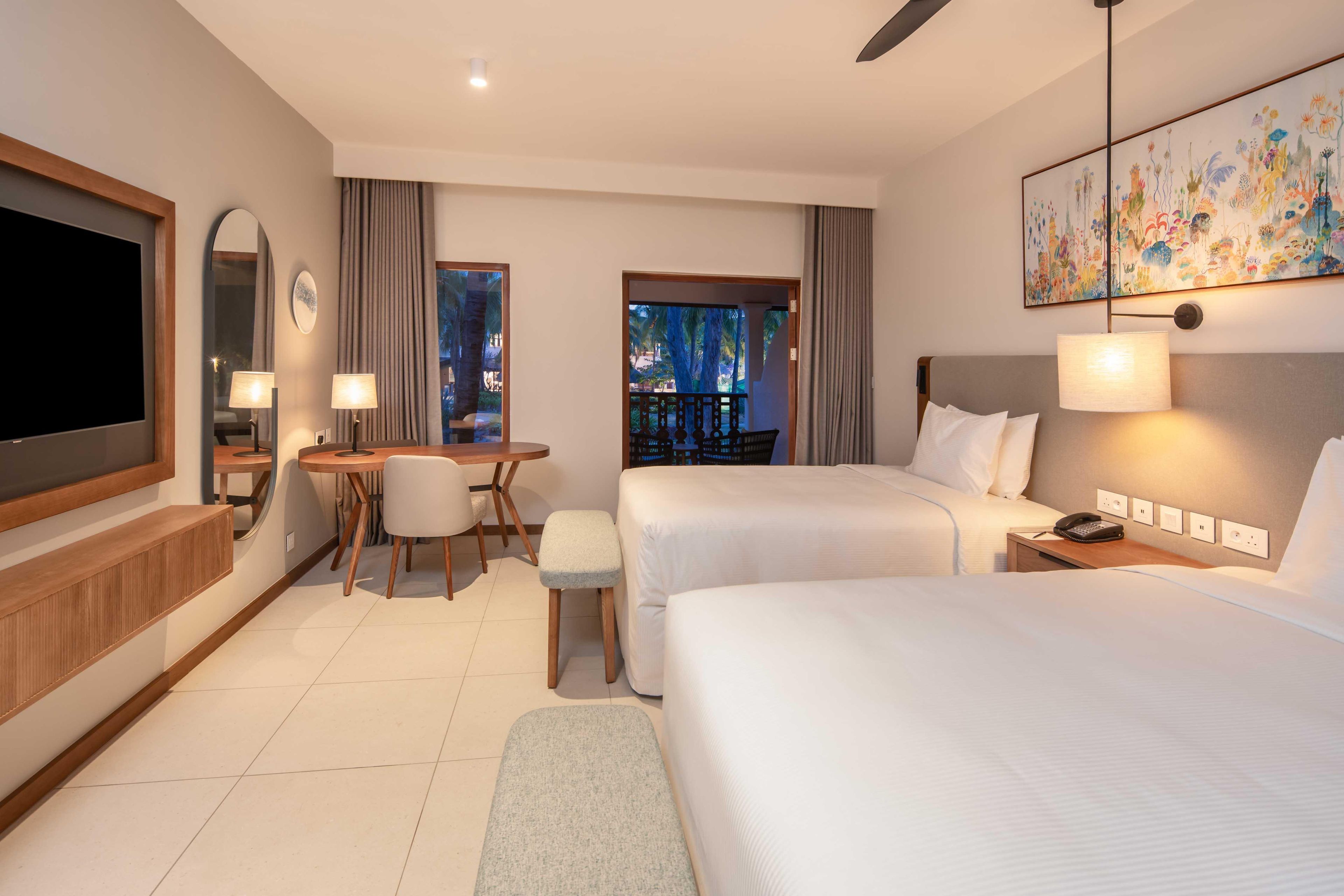 A hotel room with two beds, a desk with a chair, a TV, and a painting on the wall.