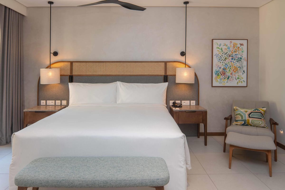 Une chambre d’hôtel avec un grand lit, des lampes de chevet, une chaise et une œuvre d’art accrochée au mur.