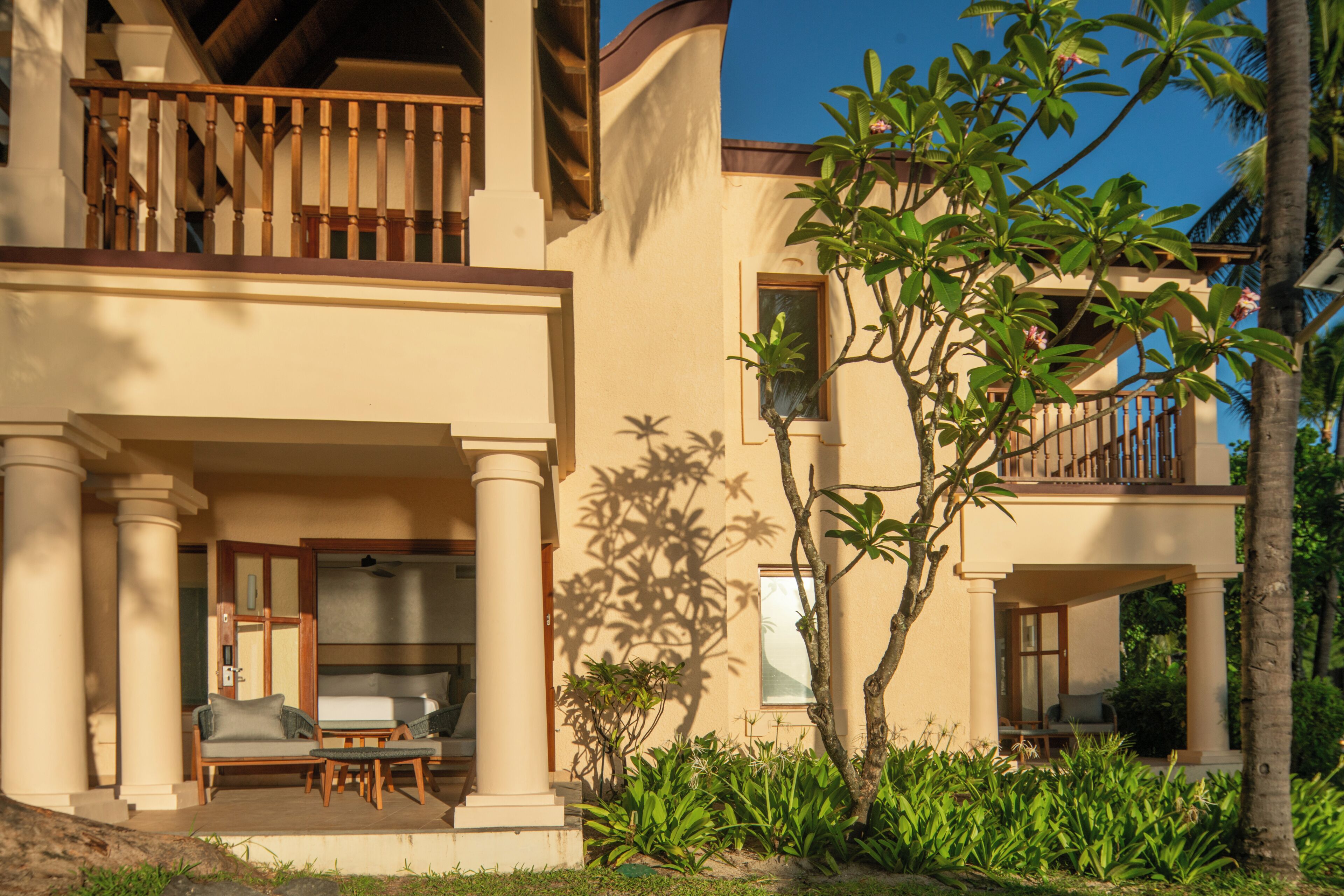 A two-story building with a balcony, a patio with seating, and lush greenery.