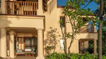 A two-story building with a balcony, a patio with seating, and lush greenery.