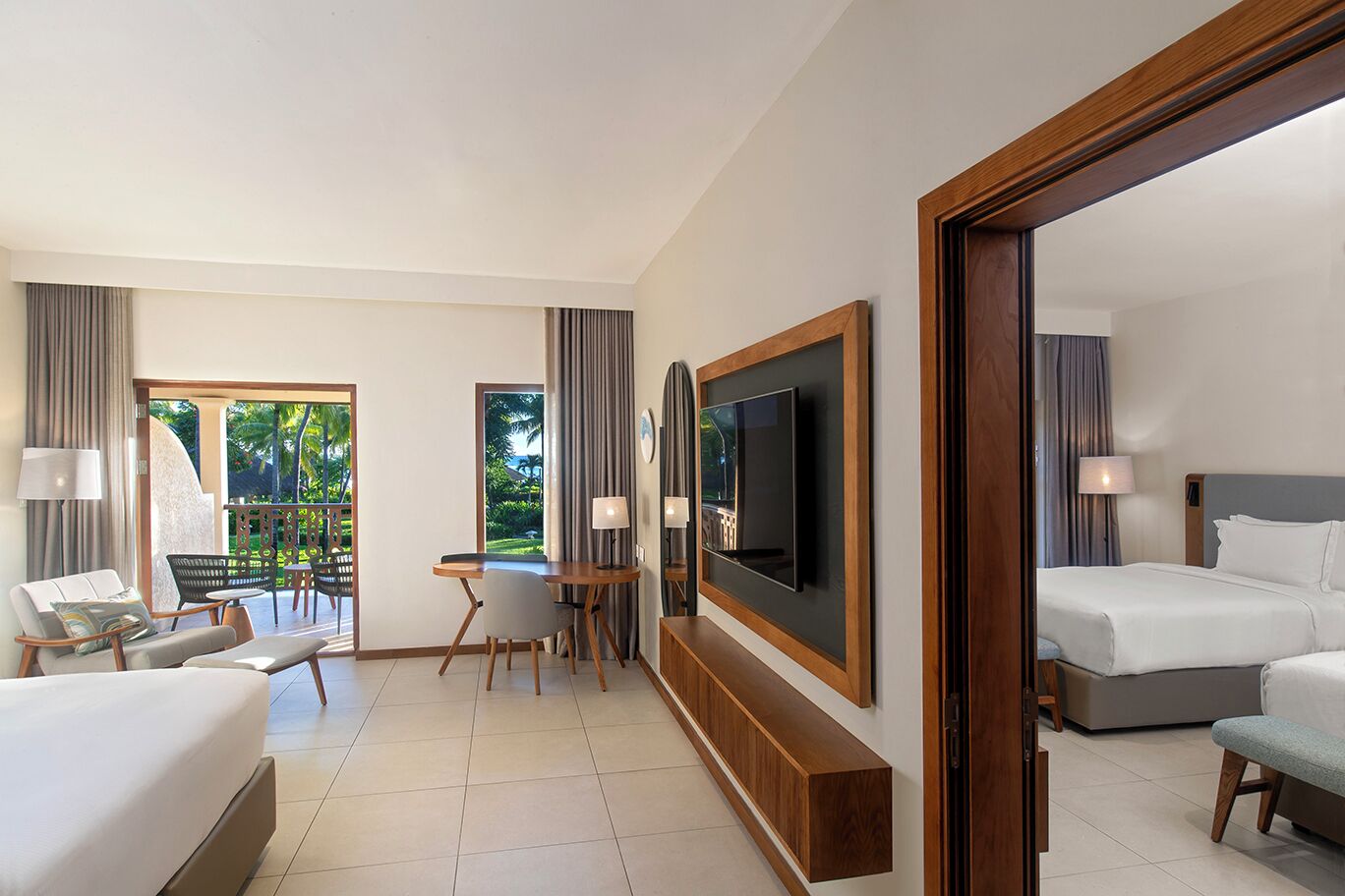 A hotel room with a bed, a desk, a TV, and a balcony with a view of greenery.