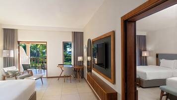 A hotel room with a bed, a desk, a TV, and a balcony with a view of greenery.