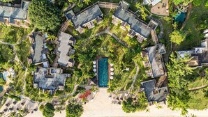 Luftaufnahme eines Resorts mit mehreren Gebäuden, einem zentralen Schwimmbecken und direktem Strandzugang.