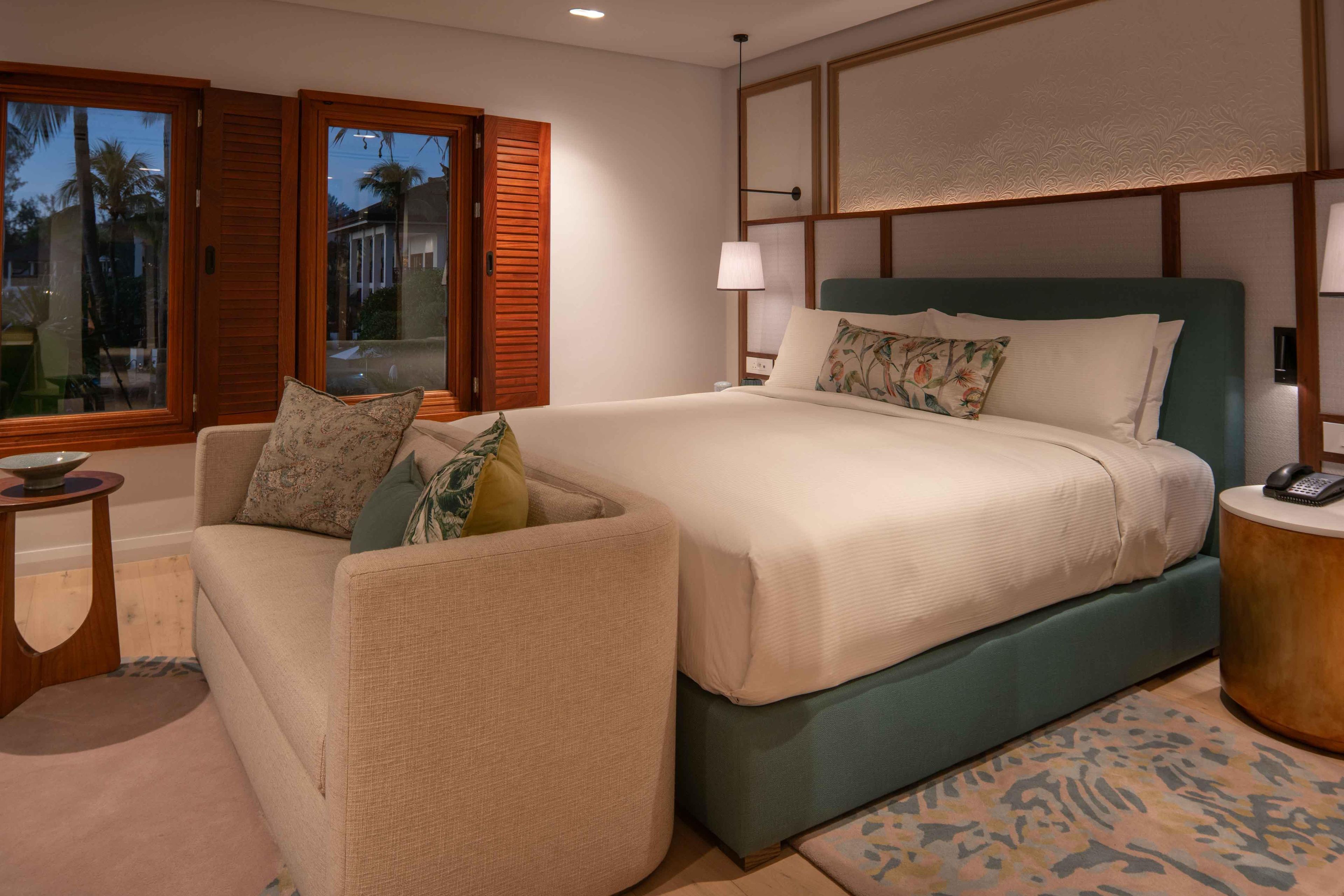 A hotel room with a bed, a sofa, a small table, and a lamp.