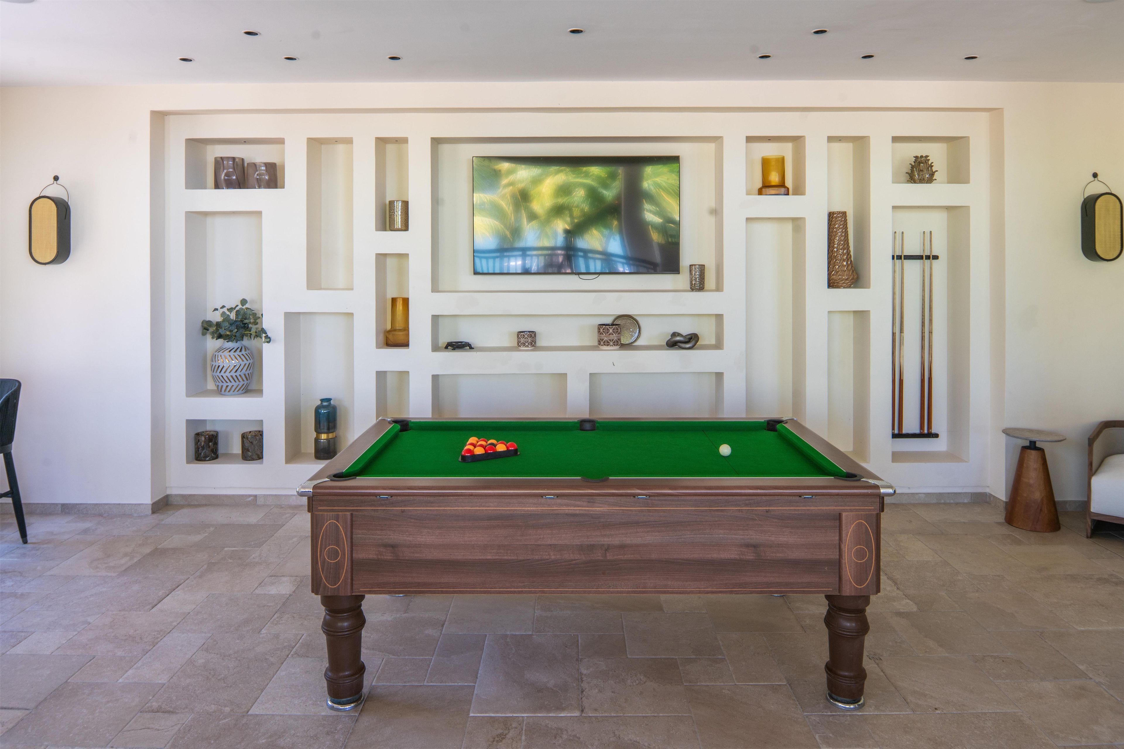 A pool table in a room with a television mounted on the wall above it.