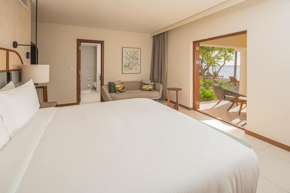 Une chambre d’hôtel avec un grand lit, un canapé, une petite table et une vue sur la plage.