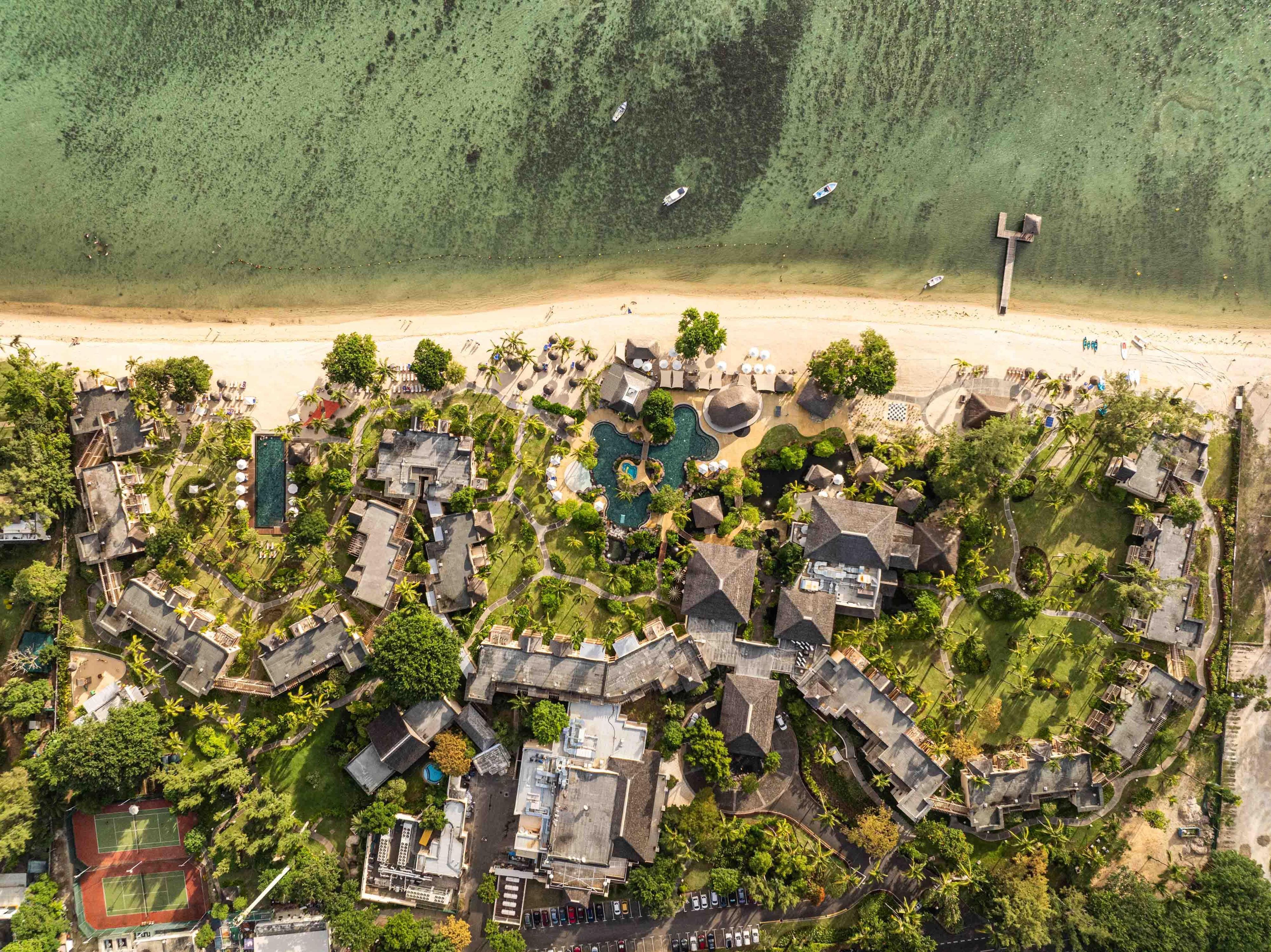 An aerial view of a resort with multiple buildings, a swimming pool, and a beach.