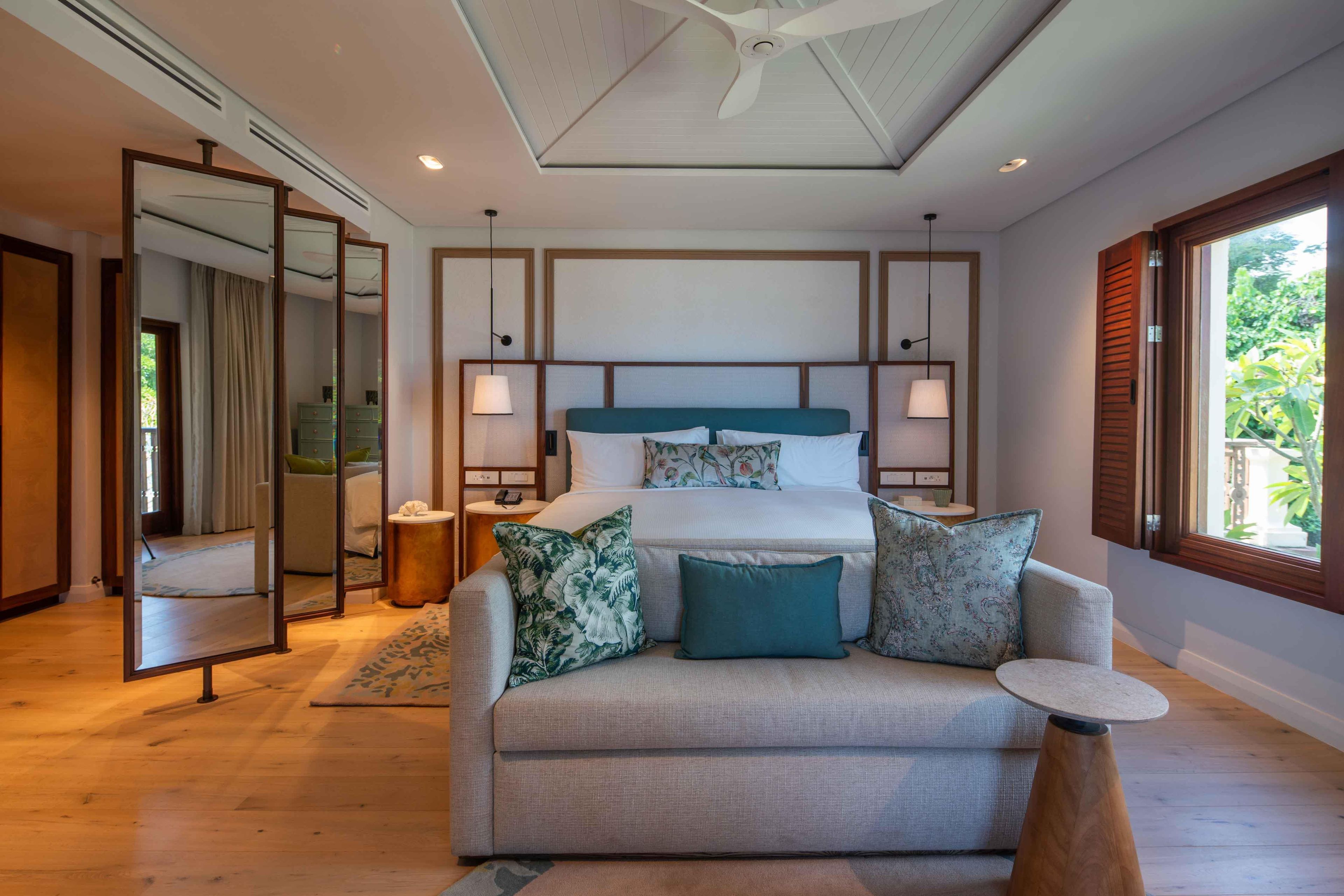 A hotel room with a bed, a sofa, a mirror, and a window.