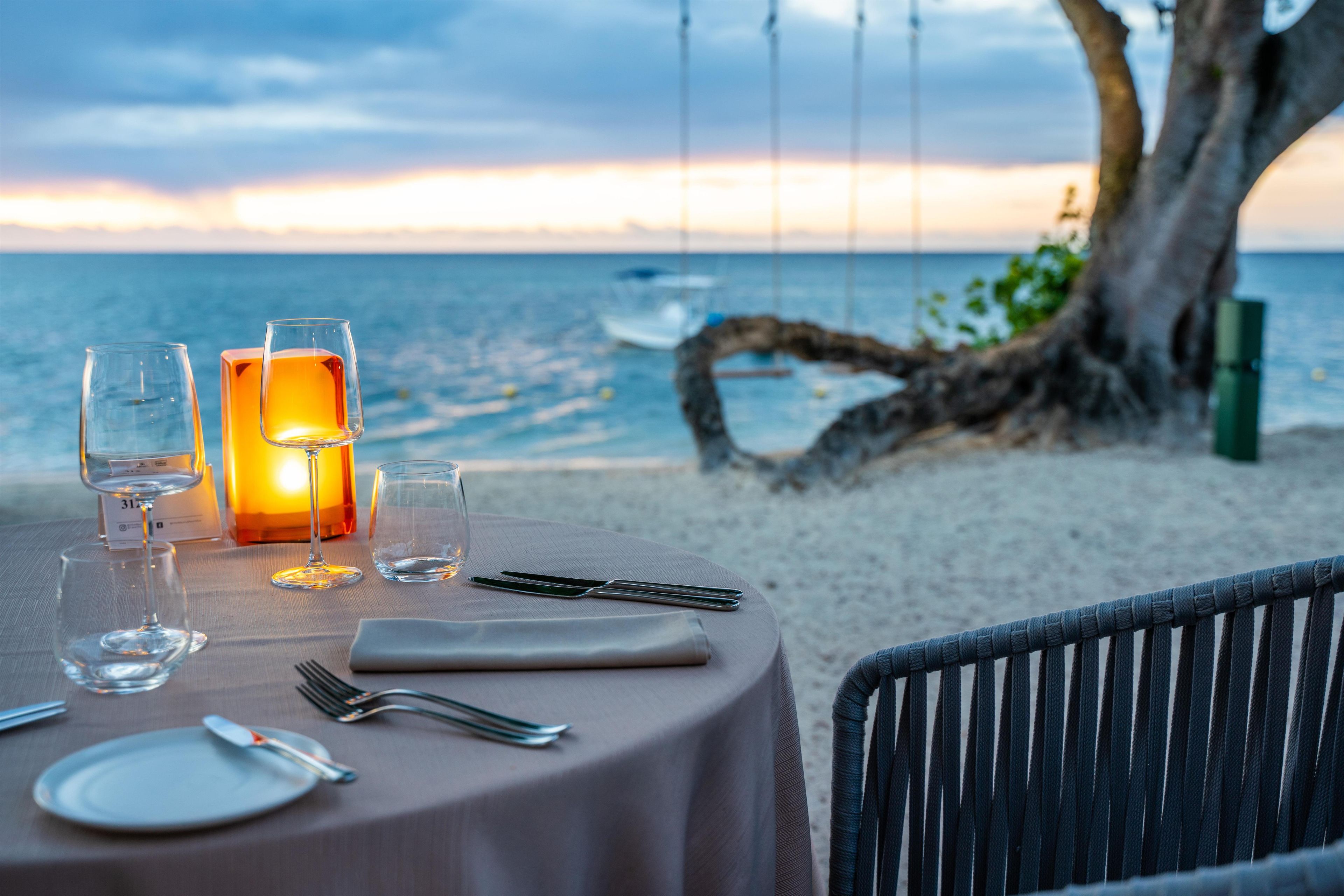 Mesa para dos con copas de vino, una vela y cubiertos, con vista al mar.