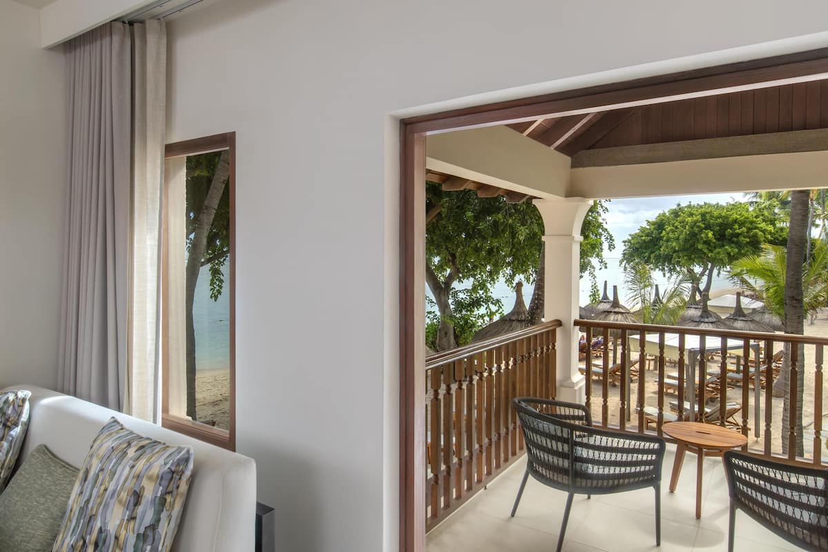 Un balcon avec vue sur la plage, un canapé blanc et un coin repas avec des chaises et des tables.