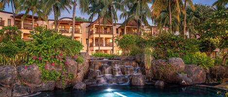 A resort with a pool, palm trees, and a waterfall.
