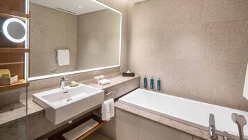 Un baño moderno con un espejo grande, dos lavamanos, una bañera y un estante con artículos de aseo.