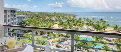 A balcony with a view of a beach, palm trees, and a pool.