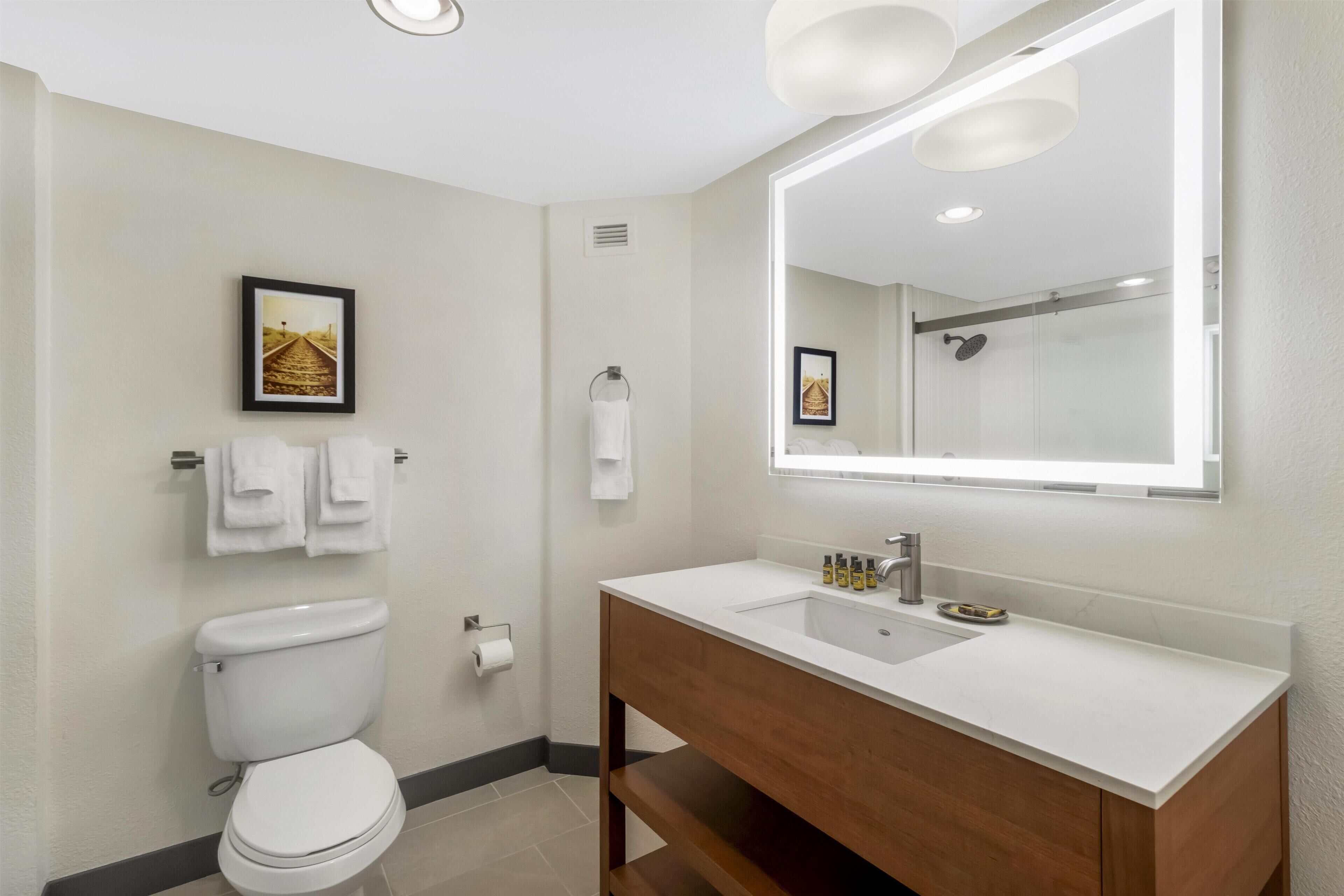 Une salle de bain moderne équipée de toilettes, d’un lavabo, d’un miroir et d’un porte-serviettes.