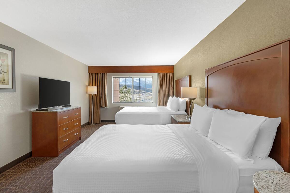 A hotel room with two beds, a television, a desk, and a window with a mountain view.