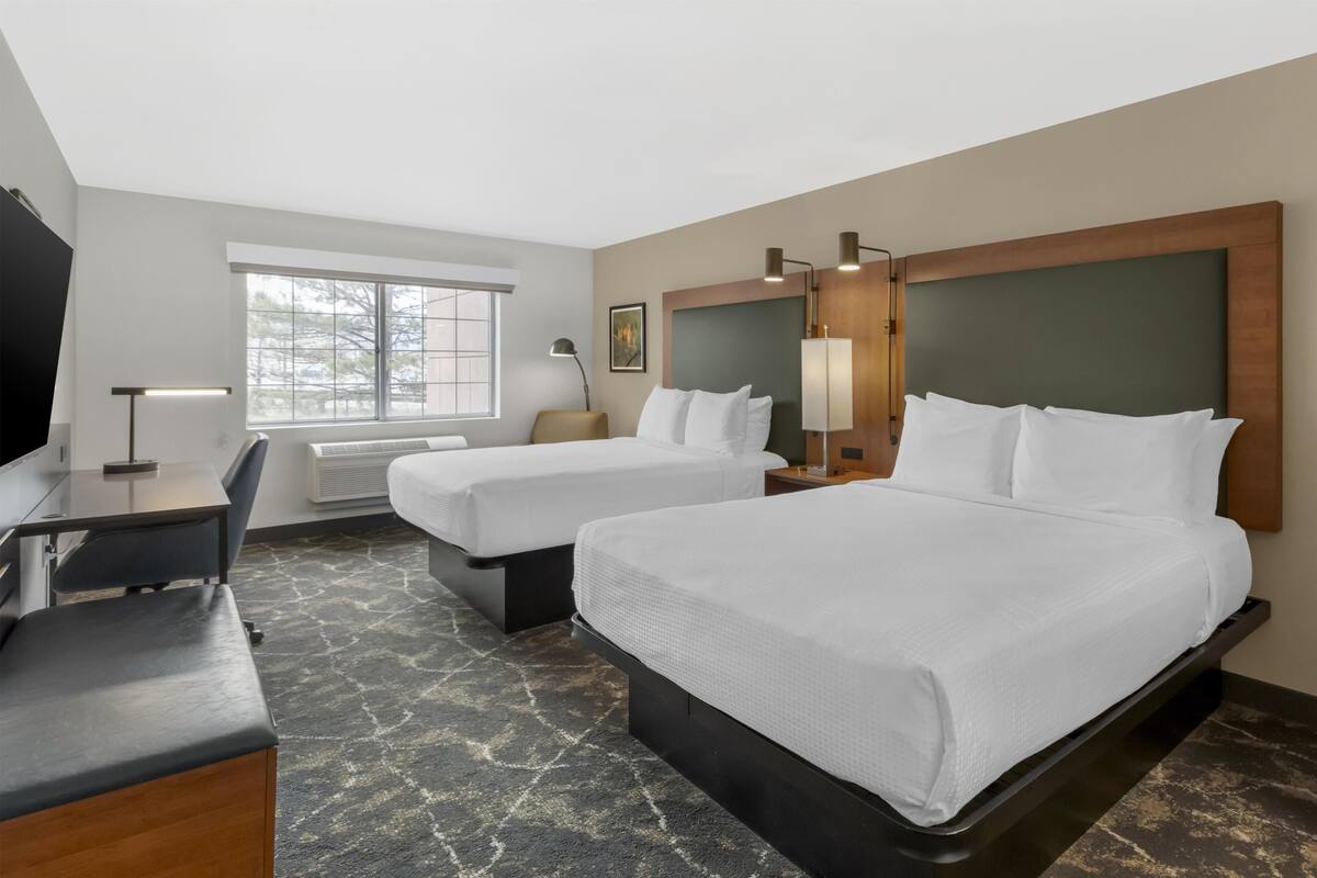 A hotel room with two beds, a desk, a chair, a TV, and a window.