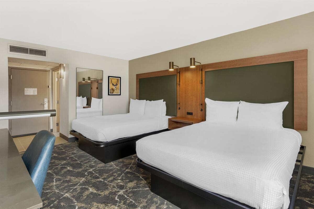 A hotel room with two beds, a desk, a chair, a mirror, and a picture on the wall.