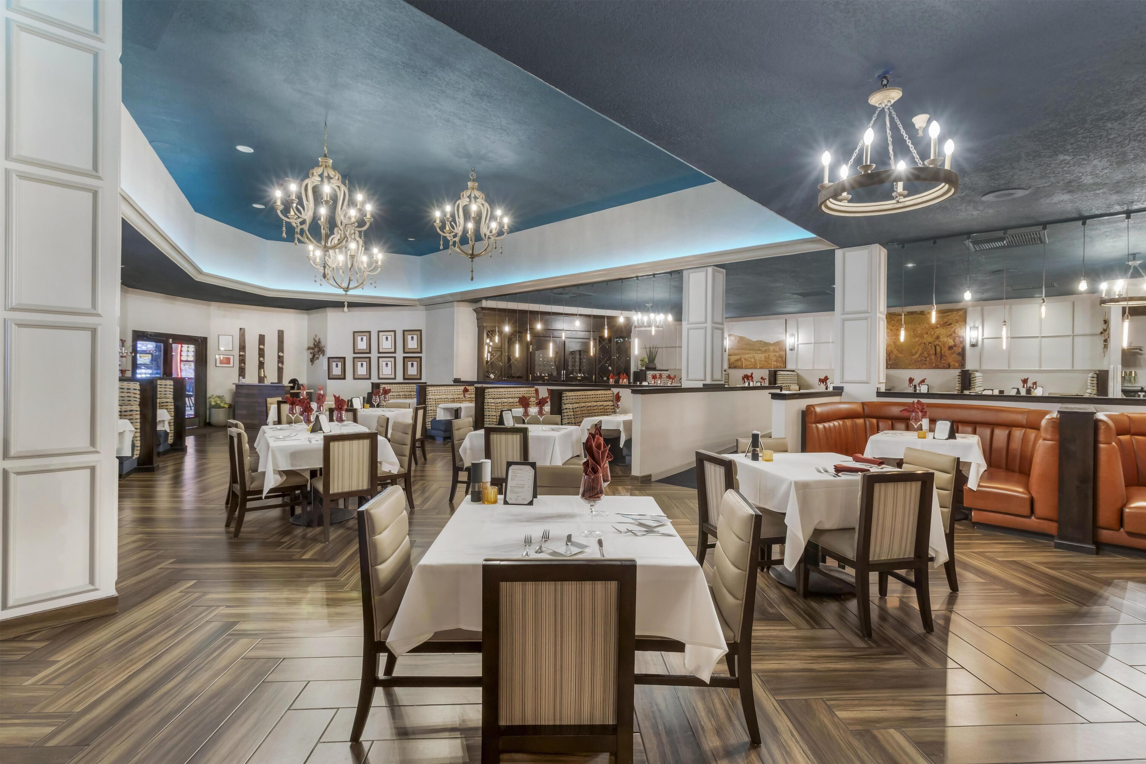 A restaurant with multiple dining areas, including a bar and seating with a high ceiling and chandeliers.