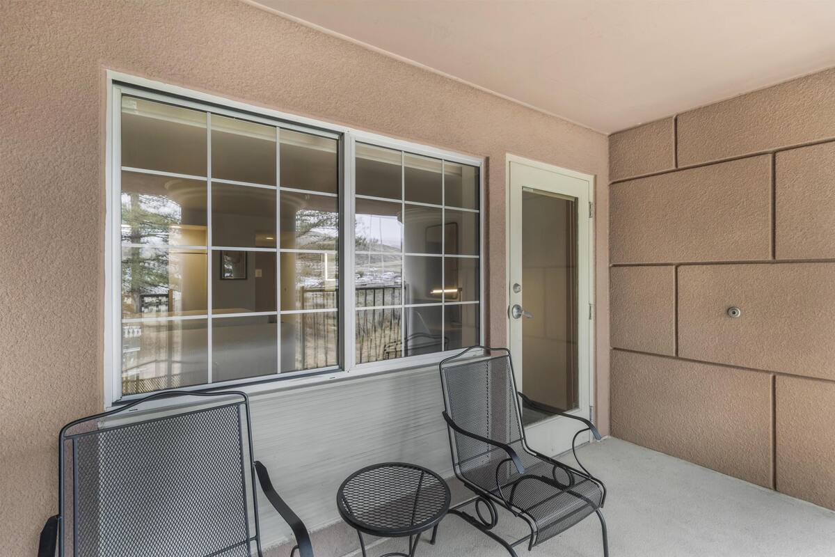A balcony with two chairs and a table, a sliding glass door, and a view of a backyard.