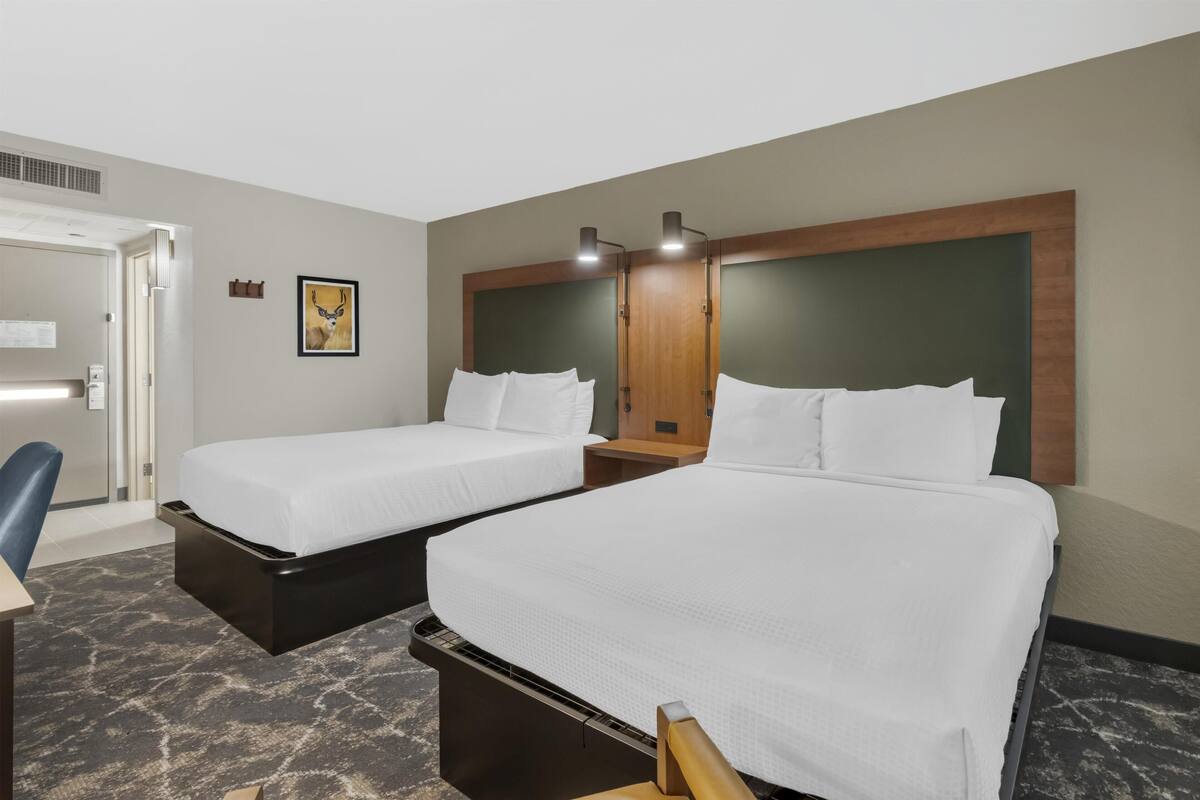 A hotel room with two beds, a desk, a chair, and a framed picture on the wall.