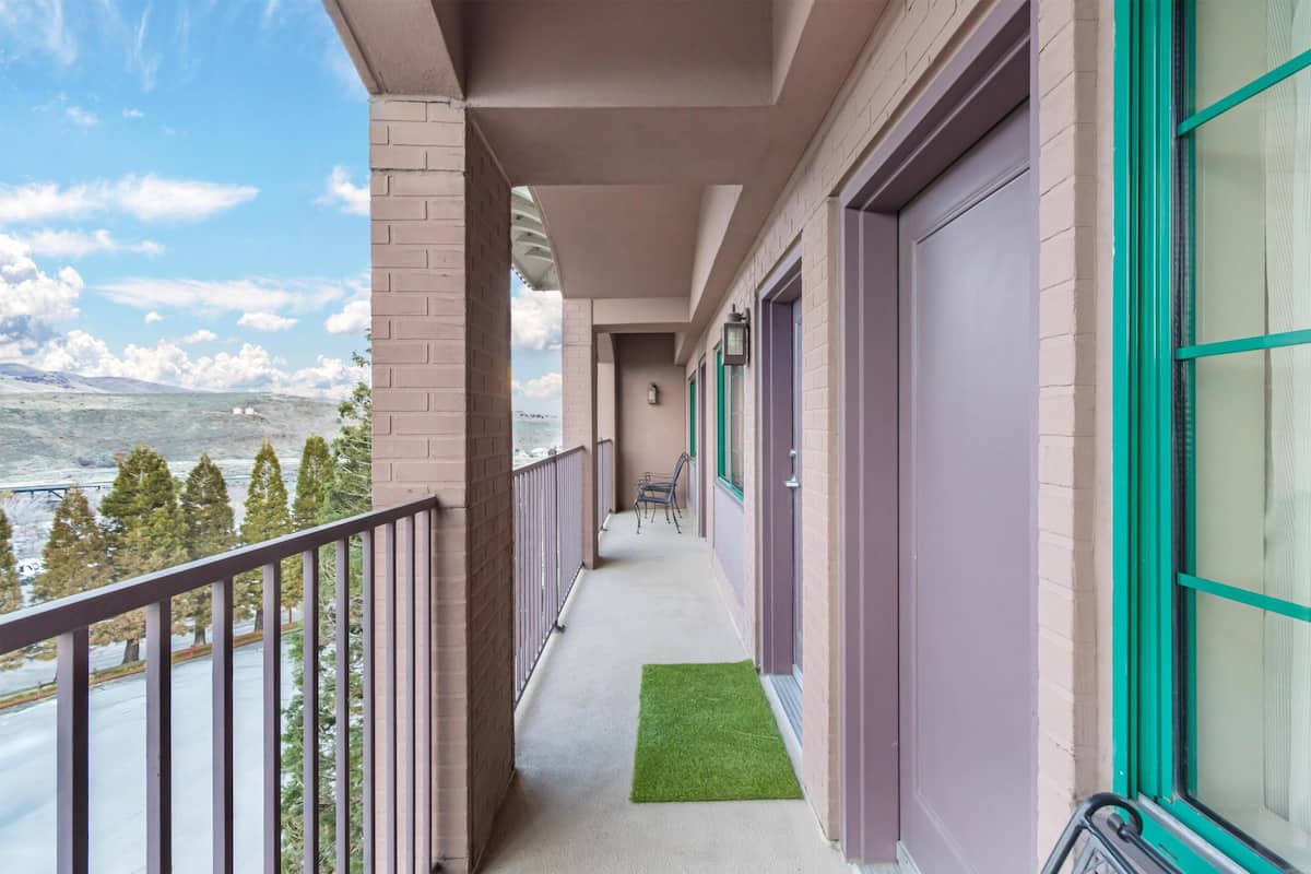 A hotel corridor with a view of a mountainous landscape, a green artificial turf, and a metal railing.