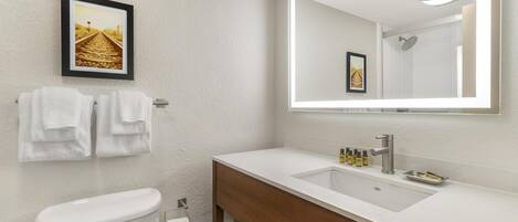 A modern bathroom with a white toilet, a wooden vanity, a large mirror, and a framed picture on the wall.