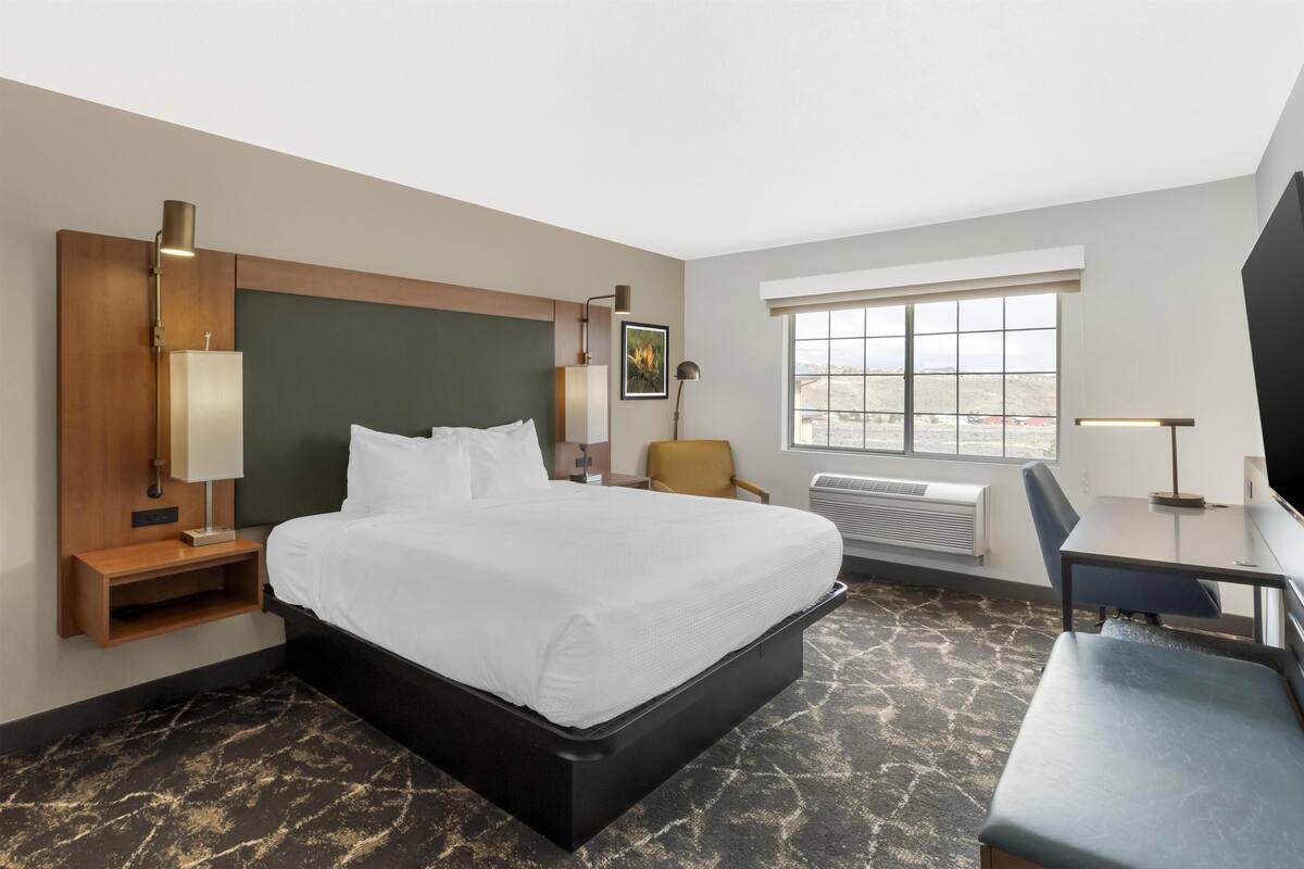A hotel room with a bed, desk, chair, bedside lamps, and a window with a view.