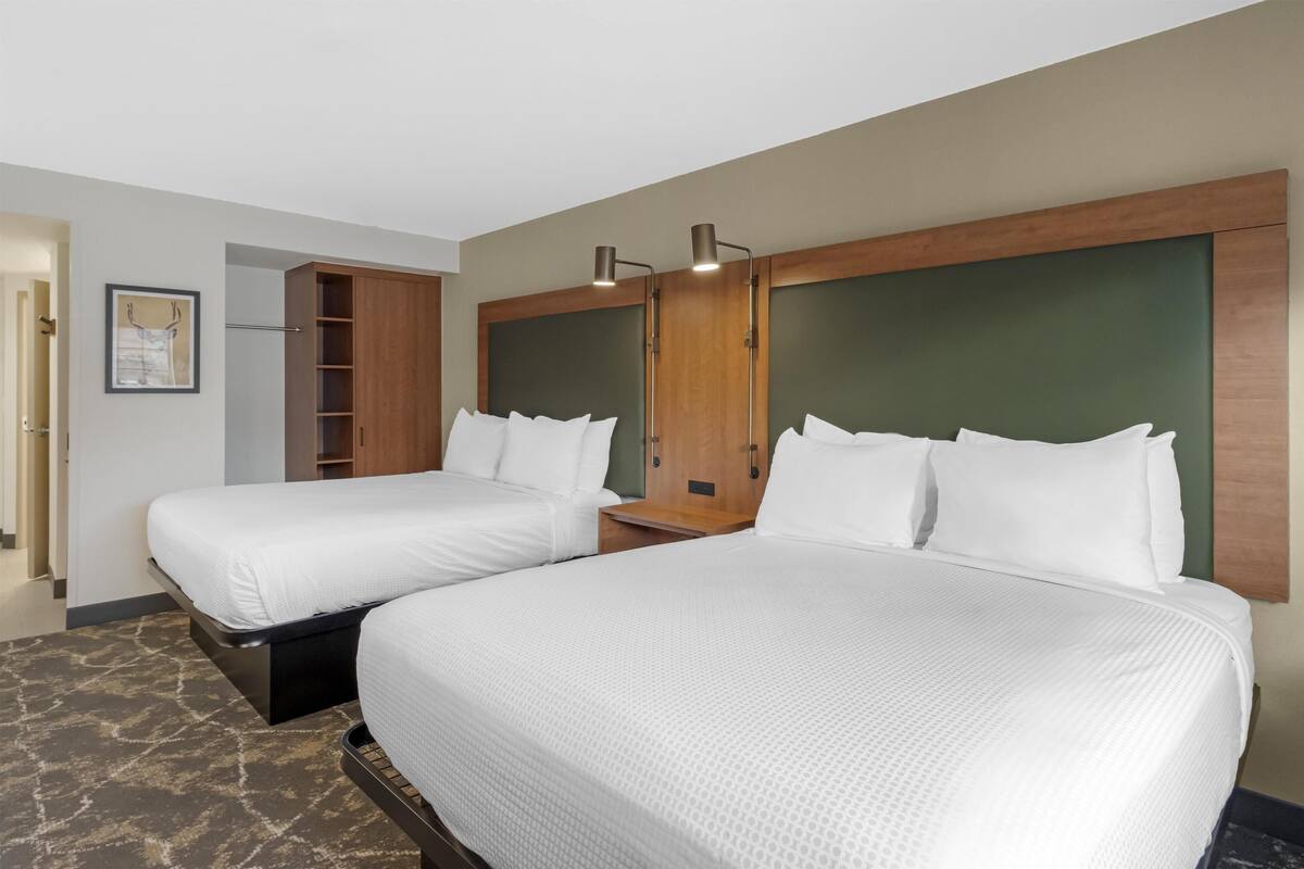 A hotel room with two beds, a wooden headboard, a small table, and a framed picture on the wall.