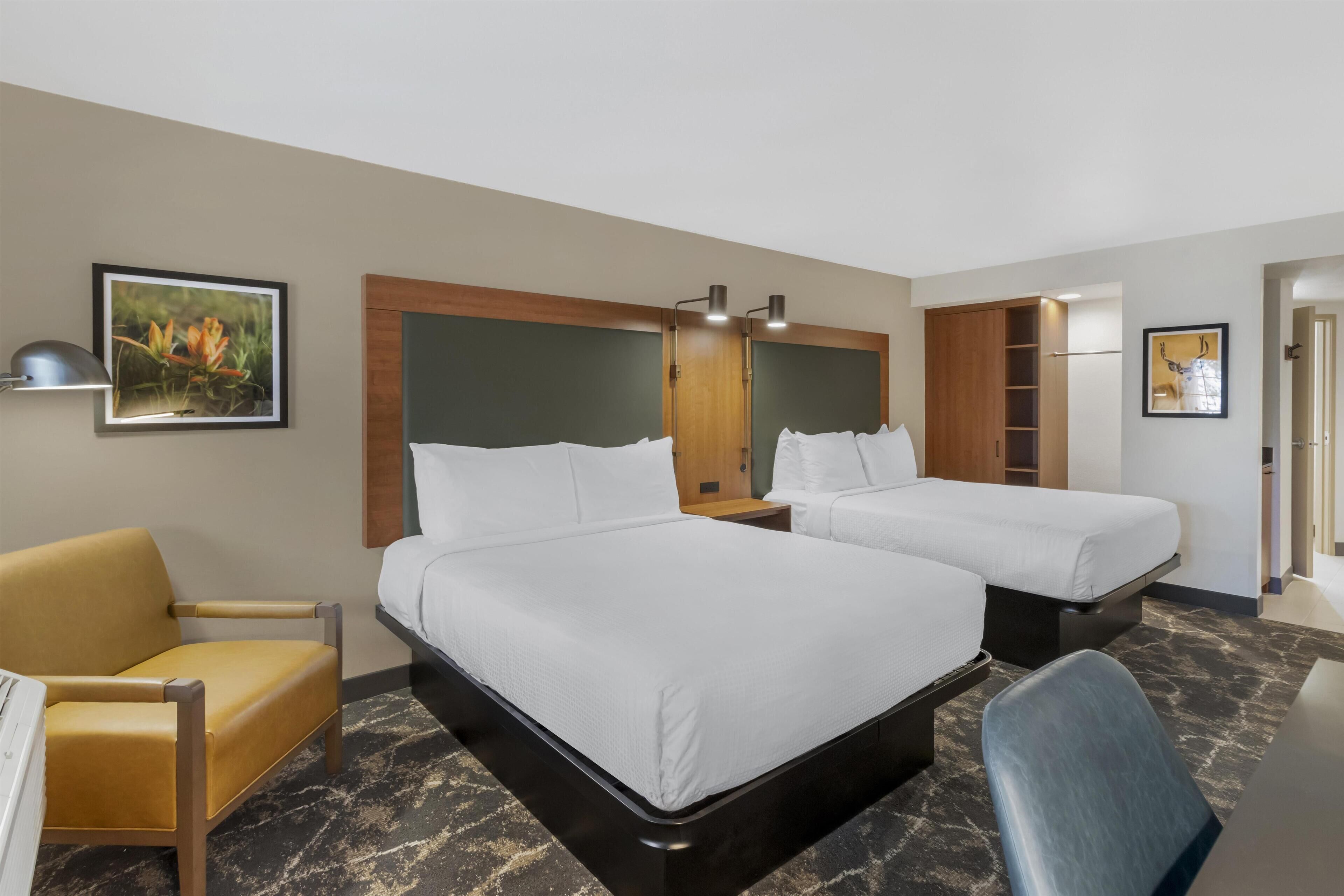 A hotel room with two beds, a desk, a chair, and a wardrobe.