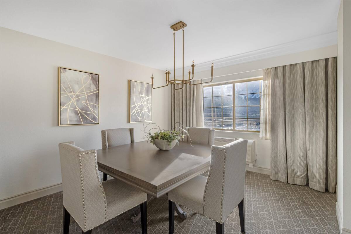 A dining room with a large table, four chairs, a chandelier, and two abstract paintings on the walls.