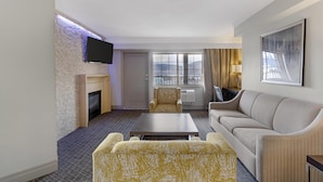 A hotel room with a fireplace, a flat-screen TV, a sofa, a coffee table, and a large window with a view.