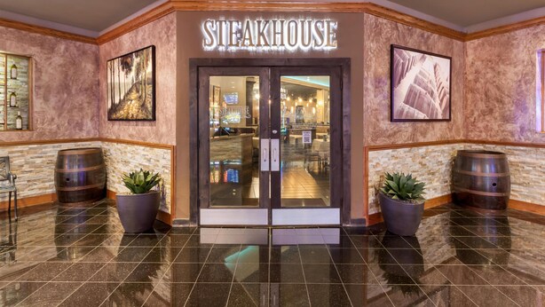 A steakhouse entrance with a sign, two potted plants, and a tiled floor.