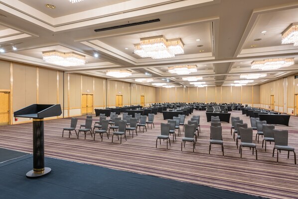Un amplio salón de conferencias con filas de sillas, un atril y candelabros.