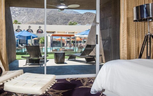 A hotel room with a bed, a view of a pool area, and a ceiling fan.