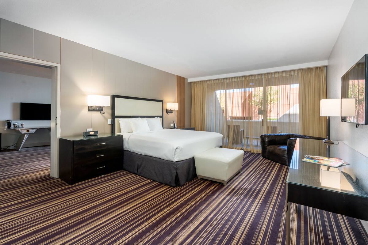 A hotel room with a large bed, a desk with a chair, a TV, and a glass coffee table.