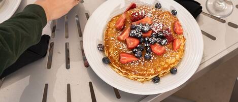 A table set with breakfast plates, including pancakes with fruit, a Bloody Mary, and a glass of orange juice.