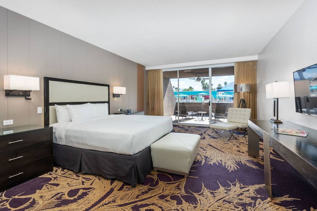 A hotel room with a bed, a desk, a chair, a TV, and a balcony with a pool view.
