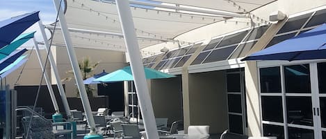 An outdoor seating area with tables and chairs, a pool with a water feature, and a covered patio area with umbrellas.