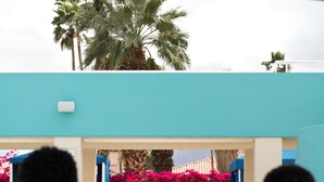 A pool area with lounge chairs and a view of a building with a blue facade and pink flowers. - Hotel Zoso (Palm Springs)