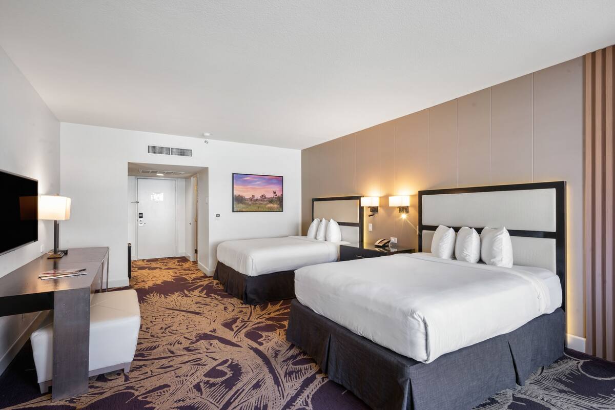 A hotel room with a large bed, a smaller bed, a desk with a lamp, a chair, and a television.