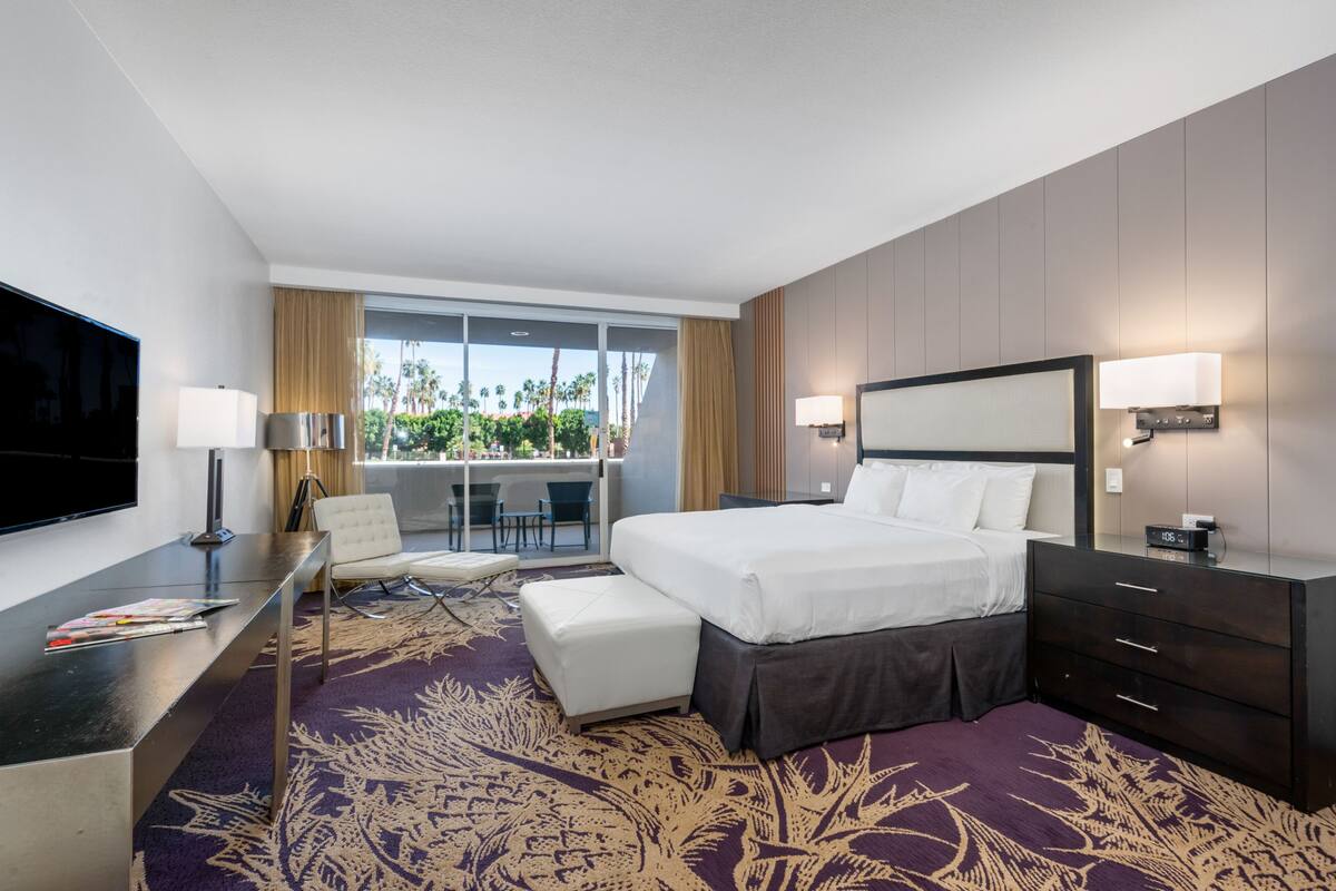 A hotel room with a bed, a desk, a TV, a balcony with a view, and a window.