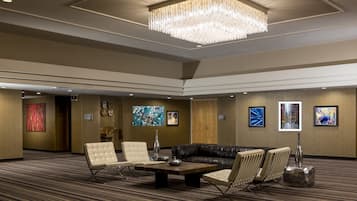 A spacious lobby with a large chandelier, leather seating, artwork on the walls, and a carpeted floor.